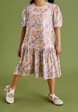 Robe fleurie avec manches bouffantes aux couleurs pastel. Réalisée en tissu pailleté. Dispose d'un ourlet à volants. Portée avec des ballerines de couleur claire.