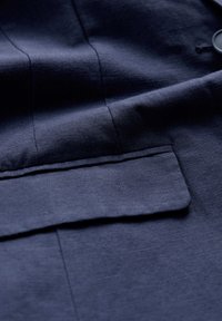 Dark navy fabric featuring a subtle texture, with visible stitching lines and a flapped pocket detail on the left side.