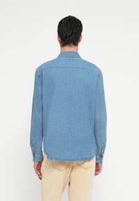 Jasnoniebieska koszula dżinsowa z długimi rękawami, mankietami na pojedynczy guzik i kołnierzykiem. Posiada przeszycie na plecach oraz lekko zaokrąglony dół.