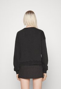 Sudadera negra de manga larga, ajuste holgado, puños y dobladillo acanalados. Combinada con una falda negra con rayas. Tejido liso y texturizado.