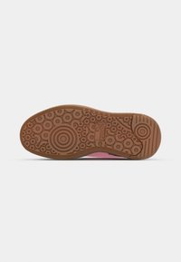 Shoe sole featuring a textured rubber bottom in brown with circular and wavy patterns; reinforced toe area and central logo detail.