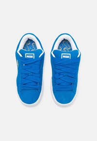 Zapatillas de ante azul con suelas de goma blancas, que presentan cordones gruesos y una lengüeta acolchada. El interior tiene un patrón geométrico.