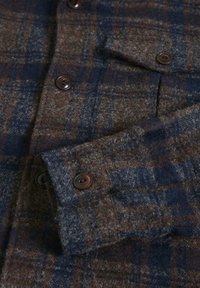 Ullflanellskjorta med ett rutmönster i brunt, grått och marinblått, med bruna knappar och en mjuk, texturerad yta.