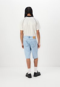 Light blue denim shorts, plain design, mid-thigh length. Short-sleeved cream checker-patterned shirt with black collar. Black shoes.