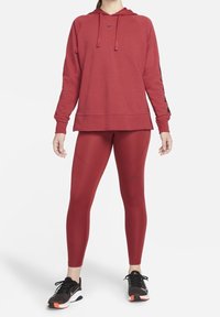 Czerwona bluza z kapturem i sznurkiem, z czarnymi akcentami, w połączeniu z czerwonymi legginsami. Obuwie ma czarno-białą stylistykę z pomarańczowymi detalami.