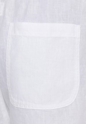 Tessuto di lino bianco con tasca quadrata cucita, fili visibili e trama naturale.