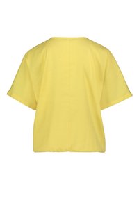 Żółta bawełniana bluzka o prostym kroju, krótkich rękawach i prostym szwie z tyłu. Materiał ma gładką strukturę.
