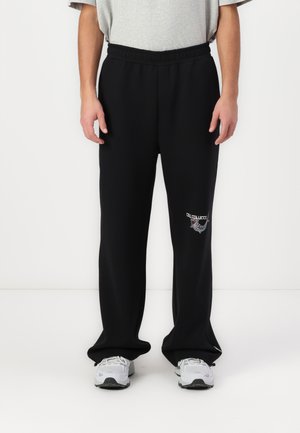 Black sweatpants with an elastic waistband, featuring a small embroidered logo detail on the left thigh. Smooth fabric with a relaxed fit.