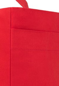 Czerwona torba tote z płaskim kształtem, z przednią kieszenią i przeszyciami. Zawiera uchwyt w pętli do wygodnego noszenia.