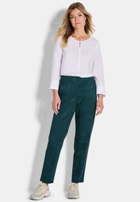 Witte blouse met lange mouwen en een keyhole-detail aan de voorkant, gecombineerd met donkergroene, taps toelopende broek van zachte, gestructureerde stof.