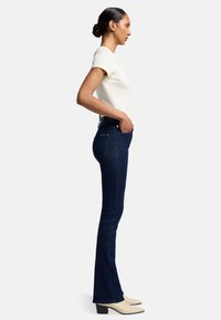 Jeans svasati di colore blu scuro con vita alta e tasche frontali, abbinati a una t-shirt attillata di colore crema e stivaletti beige alla caviglia. Texture denim liscia.