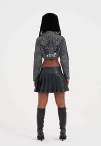 Cropped gray leather jacket with eagle graphic and 1971 design, paired with a black pleated mini skirt and knee-high black boots.