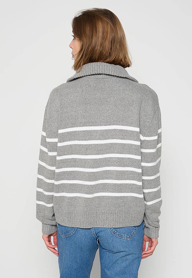 Un pull tricoté gris avec un col montant, orné de rayures horizontales blanches. Le design est ample avec des bords côtelés aux poignets et à l'ourlet.