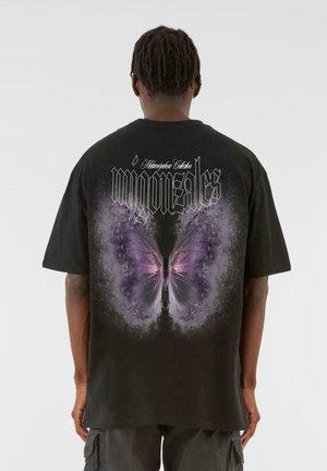 Black oversized t-shirt featuring a large purple butterfly graphic on the back, with stylized text above and an abstract design surrounding the butterfly.