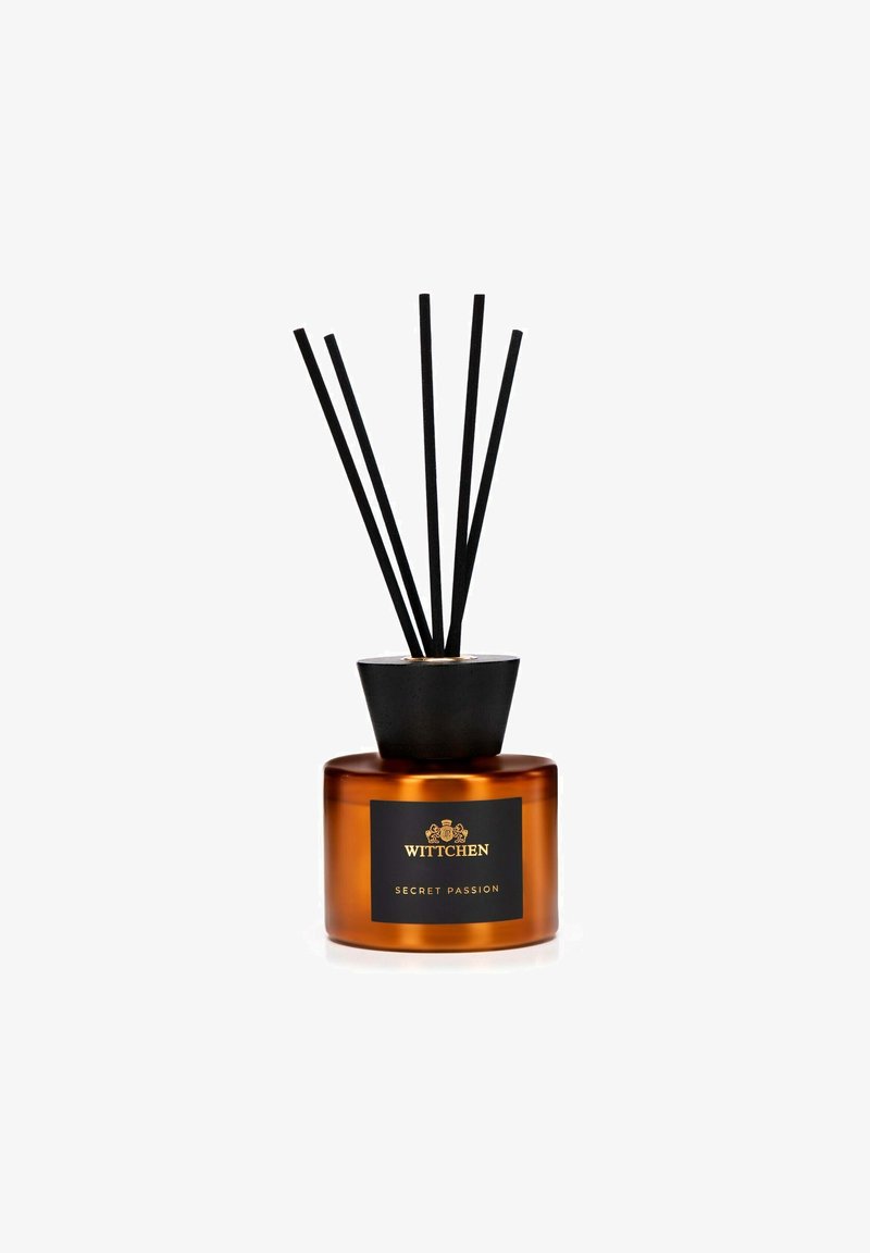 Difusor de caña en vidrio ámbar con acentos negros y logotipo. Contiene cinco cañas negras para la difusión de fragancia. Diseño suave y cilíndrico.