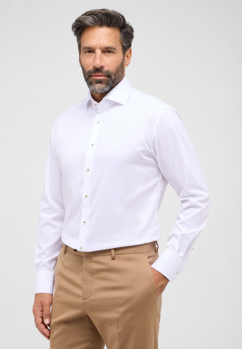 Witte gestippelde overhemdd met een spreidkraag en gouden knopen, gecombineerd met beige broek. De stof lijkt glad en gestructureerd te zijn.
