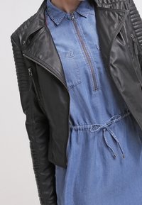 Černá kožená bunda s žebrovanými detaily na ramene, spárovaná se světle modrou denimovou šaty s límečkem a páskem na stažení v pase.