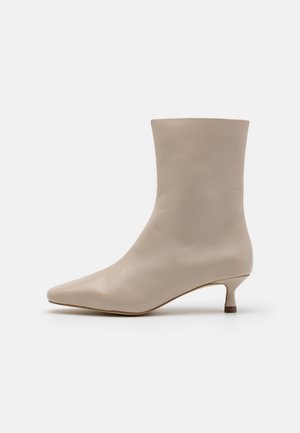 Beige læderankelstøvle med spids tå og lav kittenhæl, glat overflade, minimalistisk design på hvid baggrund.