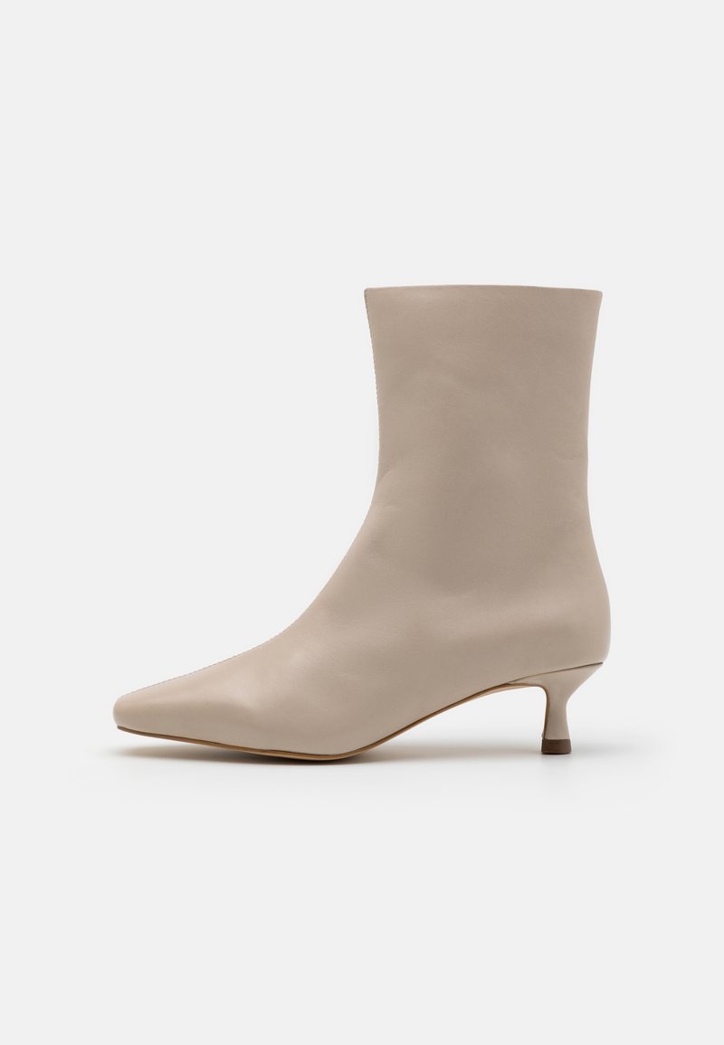 Bottine beige en cuir avec bout pointu et petit talon kitten, surface lisse, design minimaliste sur fond blanc.