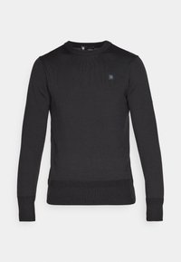 Pull en maille noire à manches longues avec un col rond, des poignets et un ourlet côtelés. Présente un petit logo sur la poitrine. Texture douce.