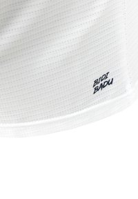Weißer Stoff mit einer strukturierten Oberfläche, versehen mit einem kleinen marineblauen Logo, das nahe dem Saum "BIDI BADU" liest, genäht für Langlebigkeit.