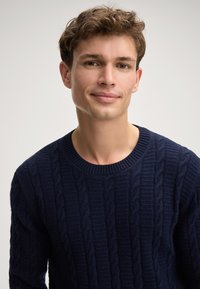 Maglione a collo giro in maglia cable-knit blu navy, con motivi in rilievo e una finitura testurizzata. Realizzato in un morbido materiale in maglia.