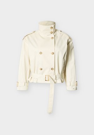 Trench-coat court de couleur crème avec col montant, fermeture à double boutonnage, taille ceinturée et brides réglables aux poignets.