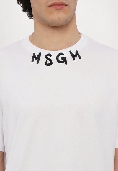 Valge puuvillane T-särk, millel on ümar kaelus, lühikesed varrukad ja mustad harjastehnikas kiri "MSGM" krae piirkonnas.