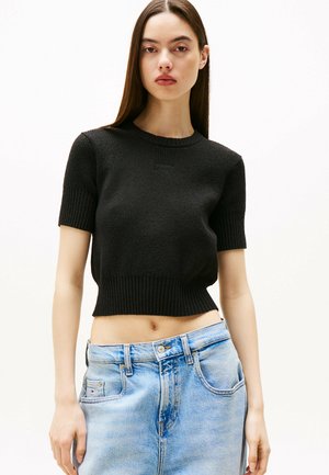 Zwarte gebreide cropped trui met een geribbelde halslijn en korte mouwen, gecombineerd met lichtblauwe high-waisted jeans. Soepele textuur.