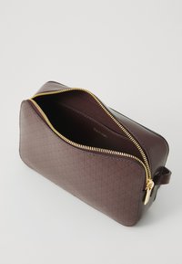 Geantă cu fermoar de culoare burgundă, cu un exterior cu model și accente din metal auriu. Interior căptușit, având numele brandului embossat.