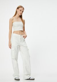 Pantaloni cargo bianchi con tasche laterali e vestibilità comoda, abbinati a un top corto a coste bianco. Il modello si trova su uno sfondo neutro.