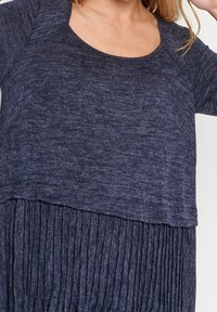 Mörkblå klänning med ett mjukt, strukturerat överlager och en plisserad nederdel, med rundad halsringning och korta ärmar.