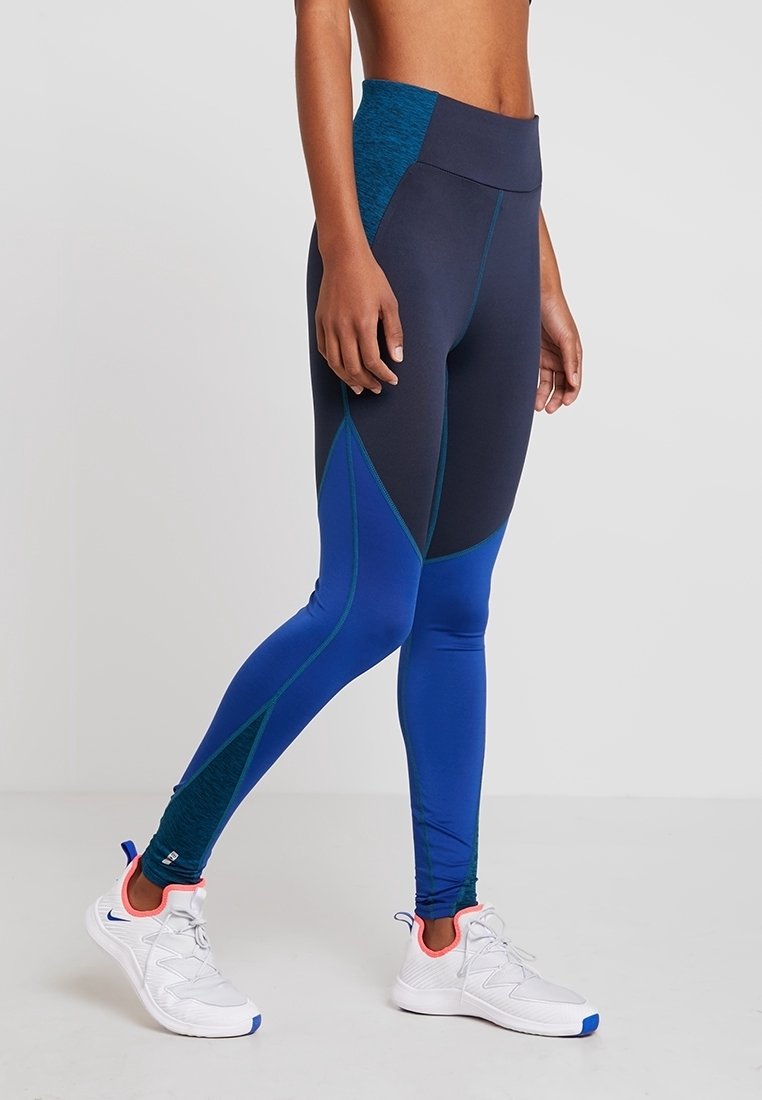 Leggings sportivi blu e navy con vita alta, design geometrico a blocchi di colore, texture liscia e accenti a contrasto.