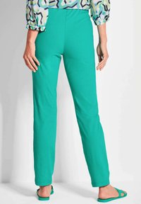 Türkise Slim-Fit-Hosen aus weichem Stoff, mit glatter Textur und elastischem Bund. Kombiniert mit passenden Flip-Flops für einen abgestimmten Look.