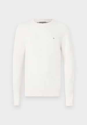 Suéter blanco de punto con manga larga, escote redondo y un sutil patrón texturizado. Presenta un pequeño logo en el pecho.