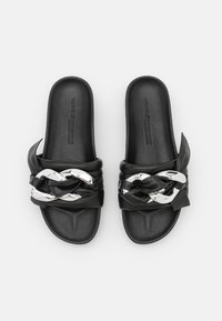 Svarta tofflor i läder med en flätad rem som har en metallkedjedetalj. Slät läderstruktur med en platt, vadderad sula.