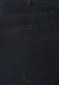 Jeans de mezclilla oscura con una textura suave, que presentan un bolsillo trasero y un sutil logotipo bordado en el bolsillo. Corte clásico y detalles mínimos.