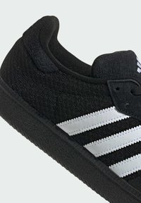 Czarne sneakersy z teksturowaną cholewką, z trzema białymi skórzanymi paskami, gumową podeszwą i wyściełanym kołnierzem dla komfortu.
