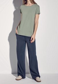 Ljusgrön, kortärmad t-shirt med rund halsringning i kombination med mörkblå, vida byxor. Avslappnade skor avslutar looken.