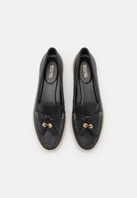 Svarta lädermockasiner med fransdetalj och guldfärgade beslag. Har kontraststickning och en platt, ljus sula.