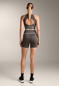 Temno siva športna obleka, ki vključuje odrezan top z izrezom na hrbtu in ujemajoče se kratke hlače visoke pasu. Okrašena z belimi črtami.