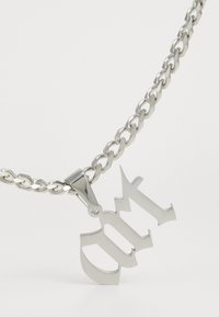 Collar de cadena de plata que presenta un colgante audaz y estilizado con letras recortadas. La cadena tiene un acabado estriado y se conecta a un colgante pulido.