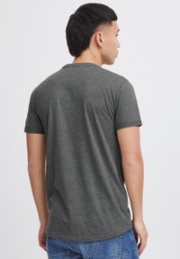 Grå kortærmet t-shirt vist fra ryggen, med en rund halsudskæring og en blød tekstur, kombineret med blå jeans.