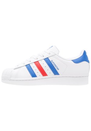 Witte lage sneaker met blauwe en rode strepen, schelpenneusontwerp en de tekst "SUPERSTAR" aan de zijkant.