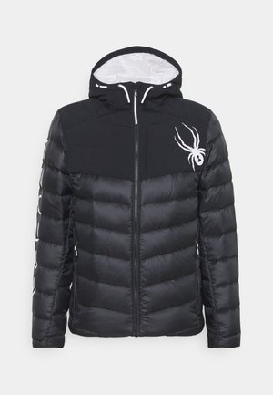 Doudoune noire avec capuche, fermeture éclair blanche, logo araignée blanc sur la poitrine et accents blancs sur les manches et la doublure de la capuche.
