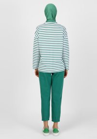 Top a maniche lunghe a righe in bianco e verde, abbinato a pantaloni verdi e scarpe bianche. Il tessuto sembra morbido con una vestibilità casual.