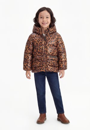 Child with dark hair wearing a brown leopard print puffer jacket, blue jeans, and brown boots, smiling and standing upright.