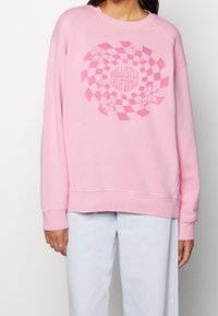 Rosa sweatshirt med rutmönster och blommiga detaljer samt texten "Hollister California" i mitten. Mjuk tyg, crewneck-design.