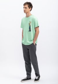 T-shirt vert menthe avec un design graphique, associée à un pantalon léger gris foncé et des baskets noires avec des lacets blancs.