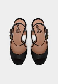 Μαύρα σανδάλια ανοιχτού δακτύλου με λουράκια στον αστράγαλο και τη φράση "LOVE MOSCHINO" τυπωμένη στις ταμπά εσωτερικές σόλες, φωτογραφημένα από πάνω σε λευκό φόντο.